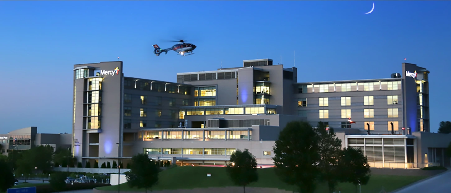mercy hospital at dusk with helicopter flying in for landing