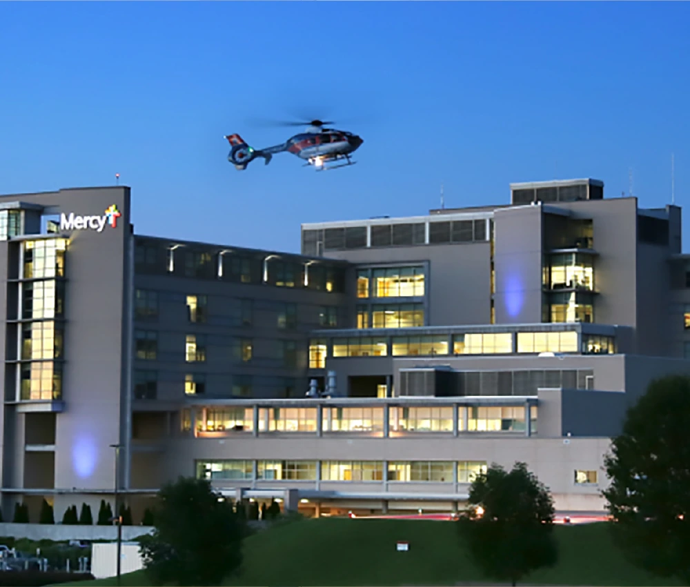 mercy hospital at dusk with helicopter flying in for landing