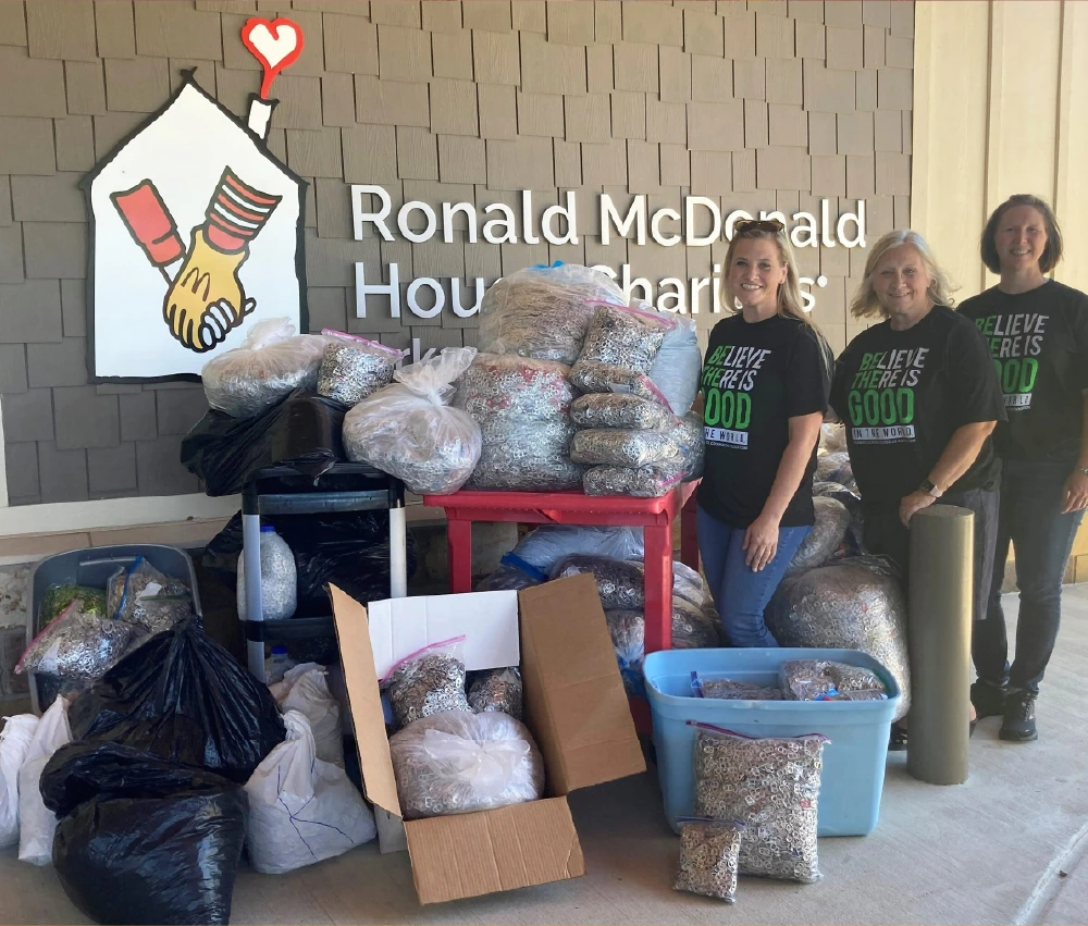 a group of volunteers standing proudly beside several bags of pop tab donations